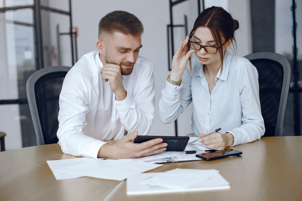 A man and woman collaborating at a desk, reviewing an online R&D finance application on a smartphone.