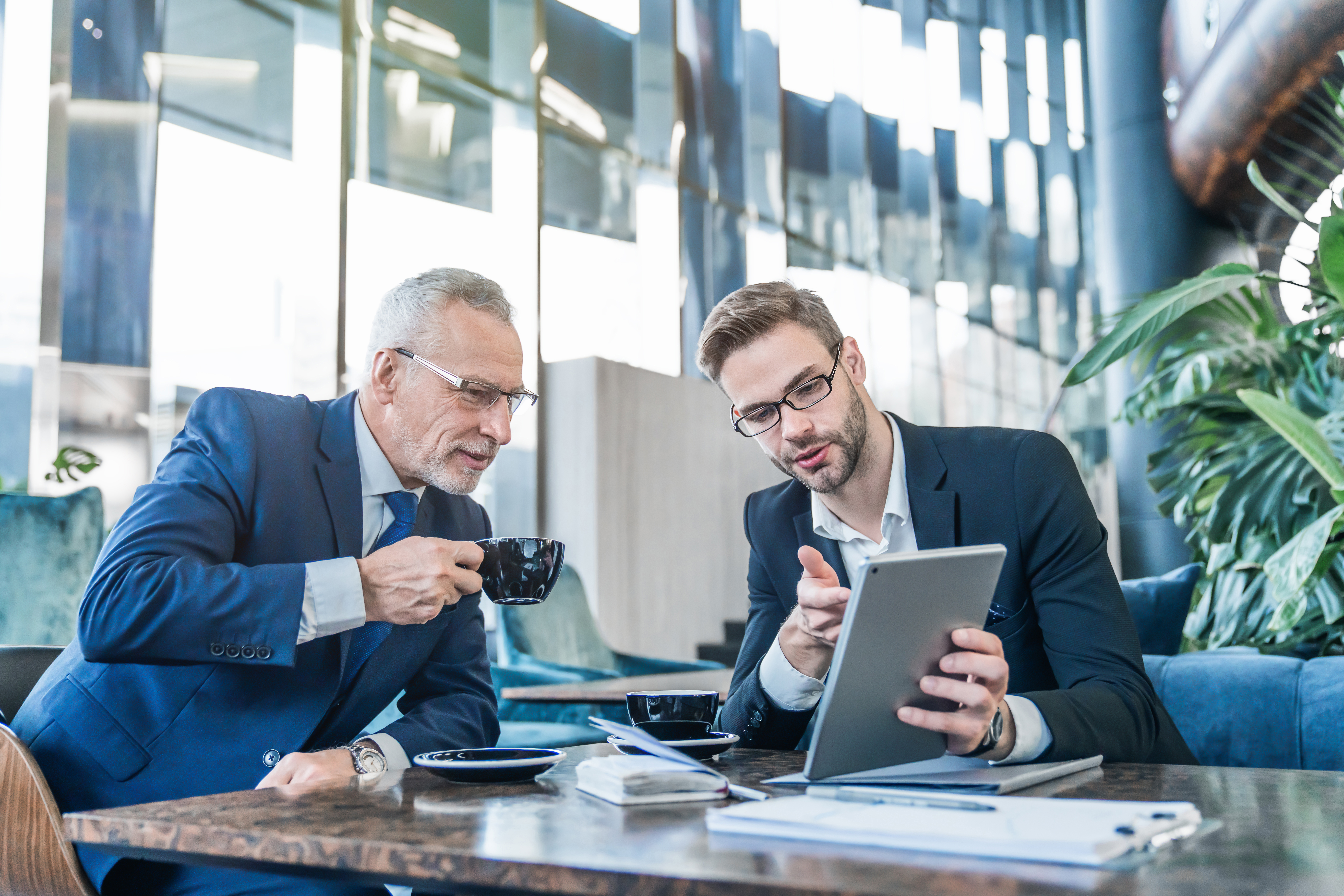 Mature boss and young business man working together using digital tablet in office hall
