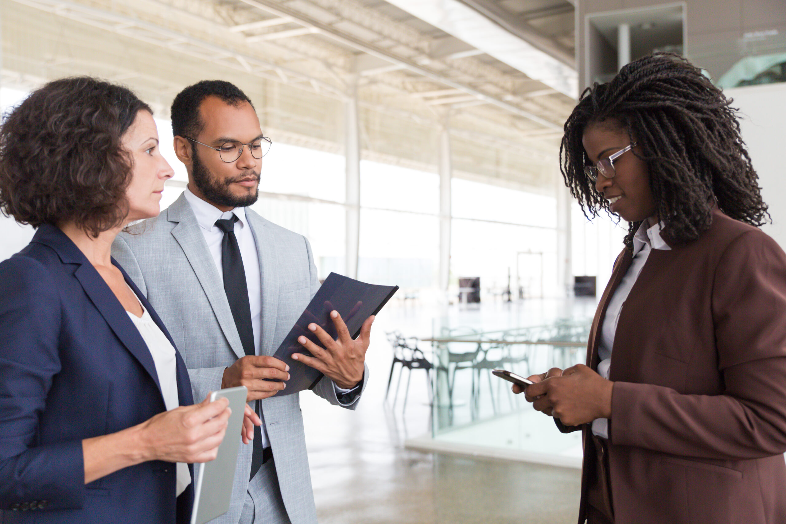 Three professionals standing together in an office space, discussing documents and a phone.