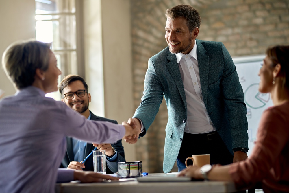 Business professionals smiling as two colleagues shake hands during a meeting.