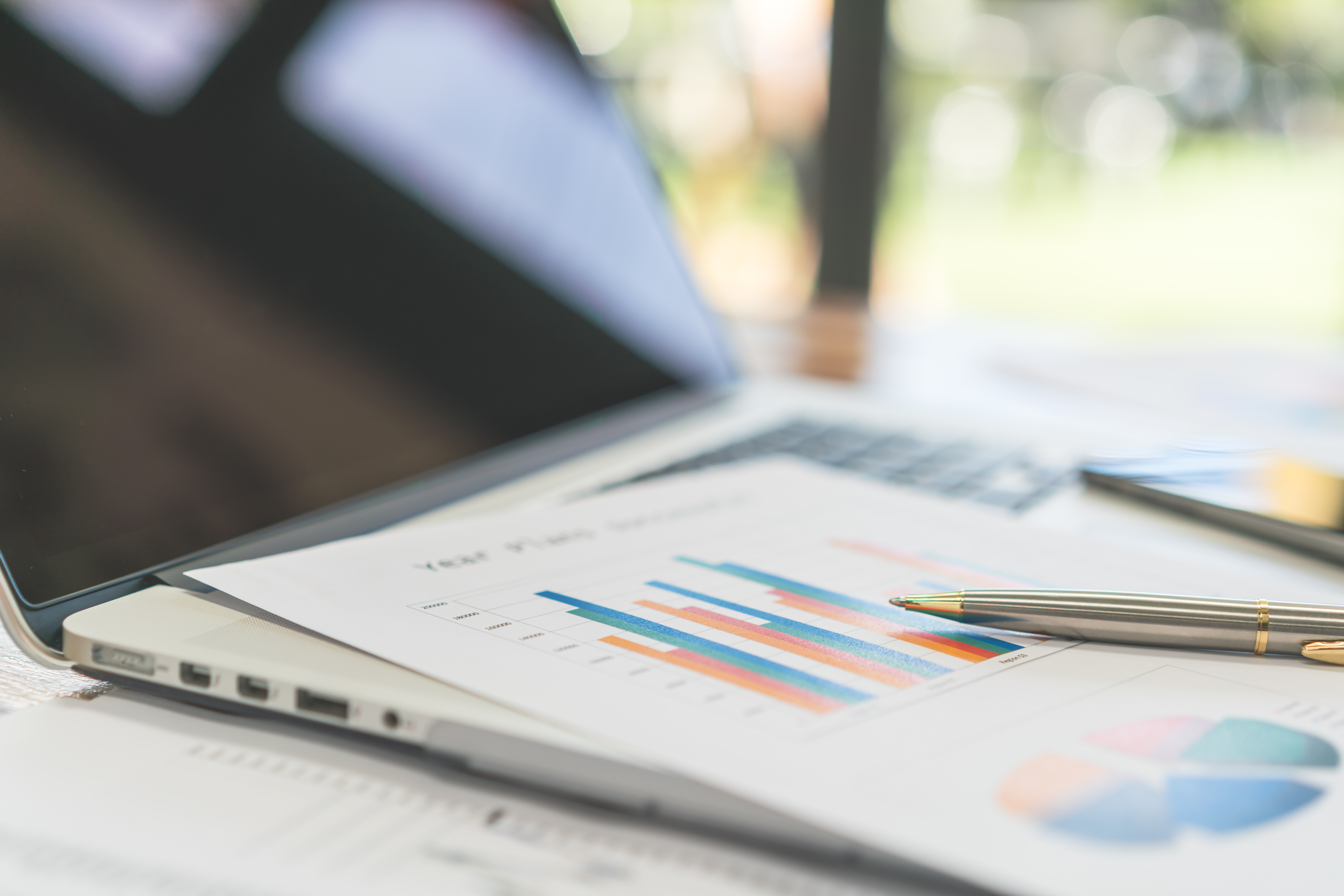 Financial charts and a pen next to a laptop, representing startup burn rate and valuation tracking.