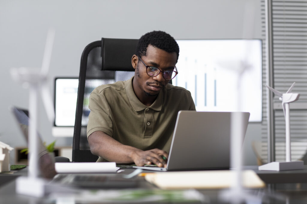 Man at a desk with miniature wind turbines working on a laptop, researching R&D tax refunds.