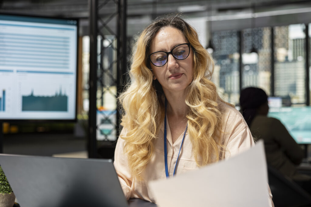 Businesswoman with glasses reviewing financial documents in an office, evaluating alternative funding sources.