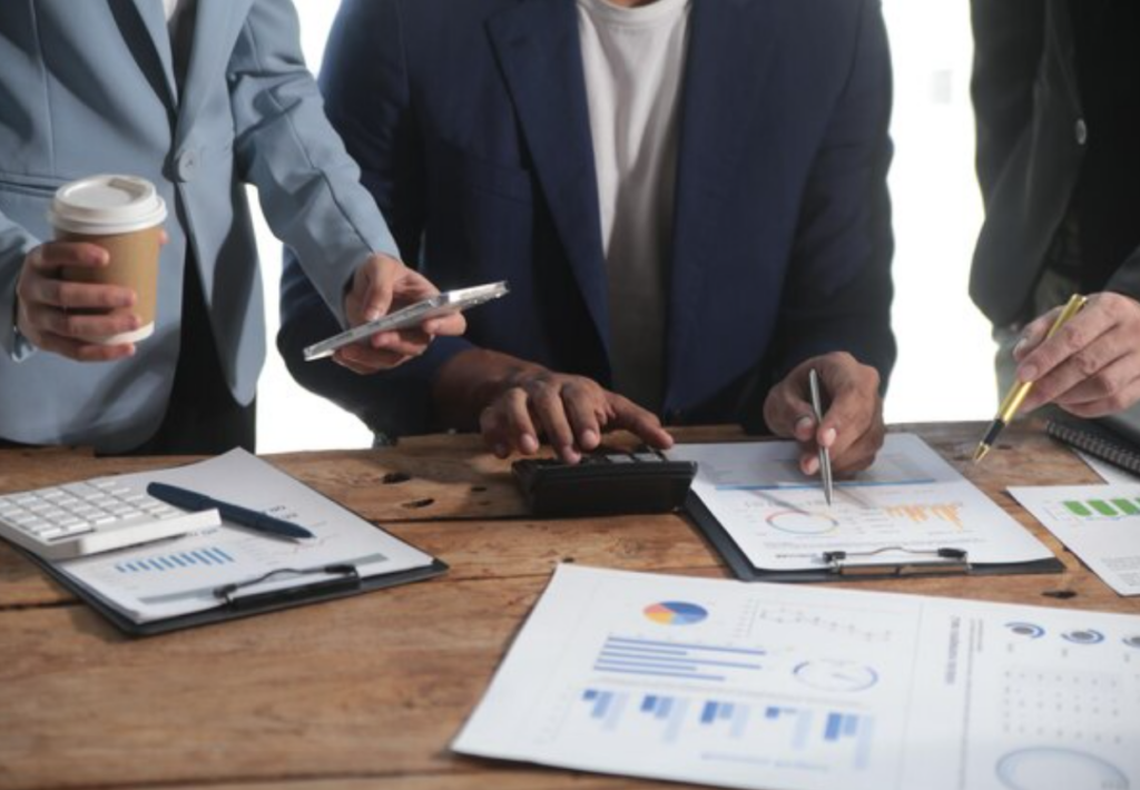 Close-up of financial specialists calculating figures and reviewing business reports at a wooden meeting table.