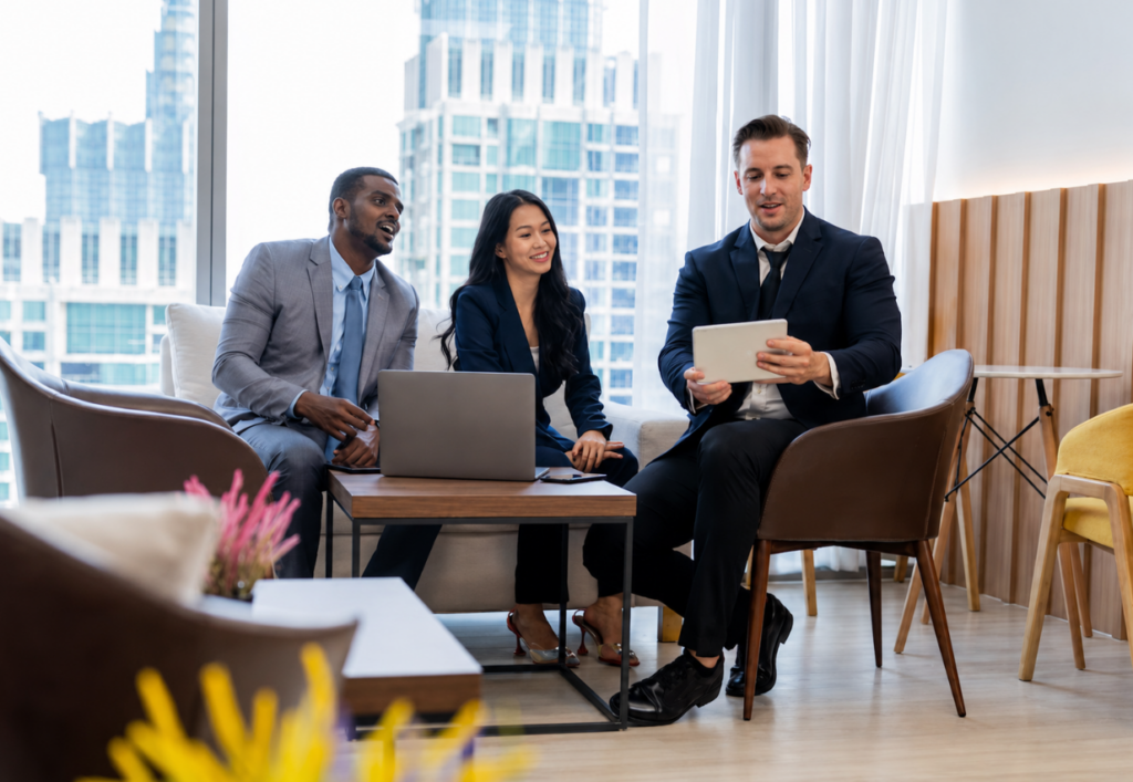 Three smiling business professionals sitting in a modern office lounge reviewing an R&D finance application on a tablet.