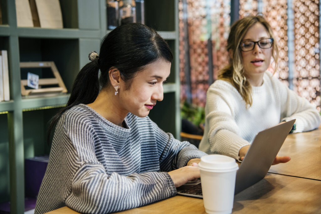 Two female colleagues collaborating on a laptop in a modern office, planning how to reinvest their R&D capital.