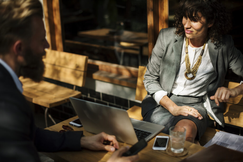 Businesswoman and a bearded man discussing 2026 Federal Budget reforms over a laptop at an outdoor cafe.