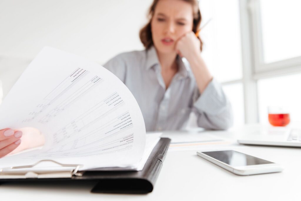 A concerned woman reviewing financial paperwork at her desk, representing the cash flow risks and disadvantages of business debt.
