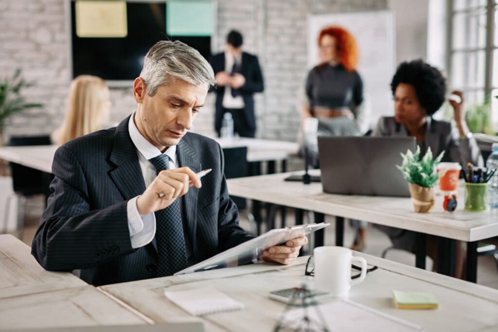 A focused businessman analyzing R&D expenditure on a clipboard in a collaborative office, representing specialized R&D finance.